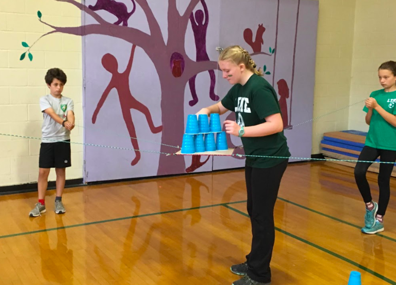 Sean, Ava, and two other students steady a platform, so Robina can add to their group’s cup stack tower. Just look at their focus!